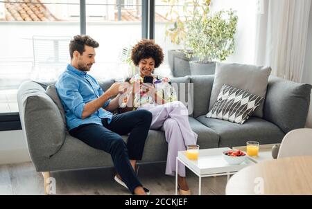 Multi-ethnic couple using smart phones while sitting on sofa in penthouse Stock Photo