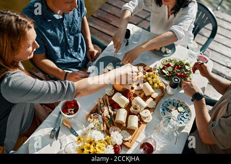 Friends having dinner with a cheese platter on jetty Stock Photo