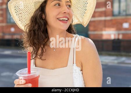 Close-up of happy young woman wearing hat holding drink in city Stock Photo