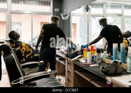 Young man relaxing on chair while barber working in hair salon Stock Photo