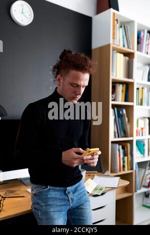 Young man using smart phone while standing at home office Stock Photo