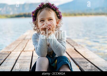 Close-up of cute girl wearing tiara laughing while sitting on jetty against lake Stock Photo