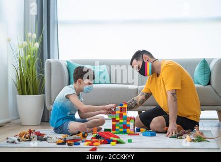 Man and boy wearing masks while arranging toy blocks in living room during curfew Stock Photo