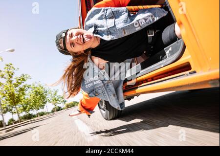 Young woman hanging from driving car, sticking tongue out Stock Photo