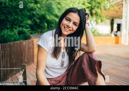 Smiling beautiful woman with hand in hair sitting at park Stock Photo