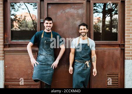 Smiling bakers in apron standing against door Stock Photo