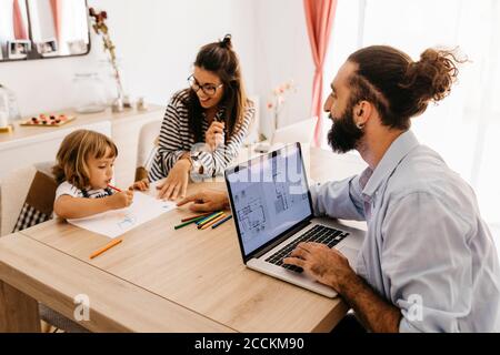Parents looking at daughter painting while working in dining room Stock Photo