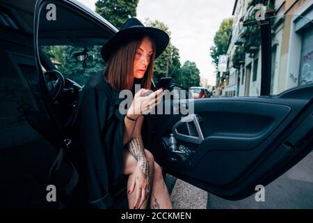 Young woman wearing hat using smart phone while sitting in car Stock Photo