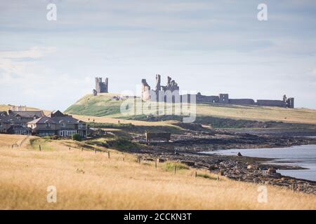 Craster village on the Northumberland coast with the ruins of Dunstanburgh Castle in the background Stock Photo