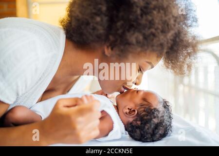 Close-up of mother kissing baby daughter lying on bed at home