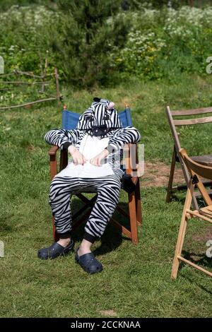 Boy wearing zebra costume sitting on chair in field during sunny day Stock Photo