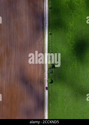 Aerial view of car driving along countryside road stretching between green and brown field Stock Photo