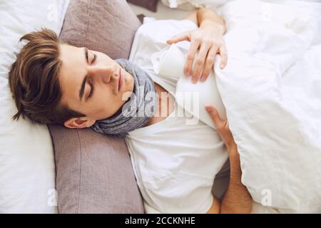 Close-up of sick young man with hot bottle sleeping on bed at home Stock Photo