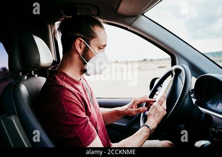 Man using smart phone while wearing protective face mask in car