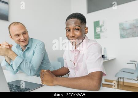 Smiling coworkers working on laptop while sitting at workplace Stock Photo