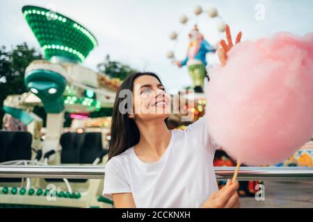 Smiling young woman holding cotton candy while standing at amusement park Stock Photo