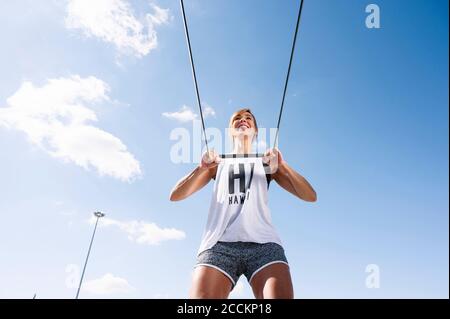 Smiling mid adult woman exercising with strap against sky during sunny day