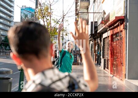 Gay couple waving hands at each other on sidewalk in city Stock Photo
