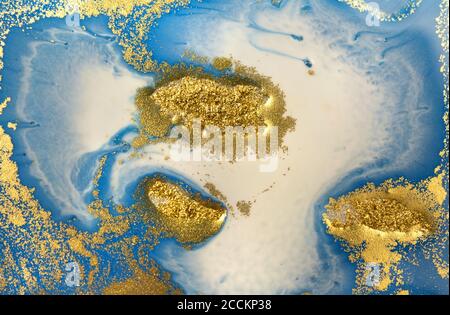 Piles of gold sequins on blue liquid ink background. Abstract pattern. Stock Photo