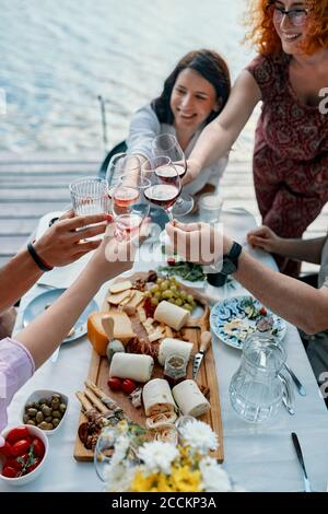 Friends having dinner at a lake clinking wine glasses Stock Photo