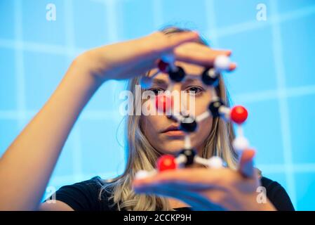 Close-up of young female scientist holding molecule model against blue grid pattern Stock Photo