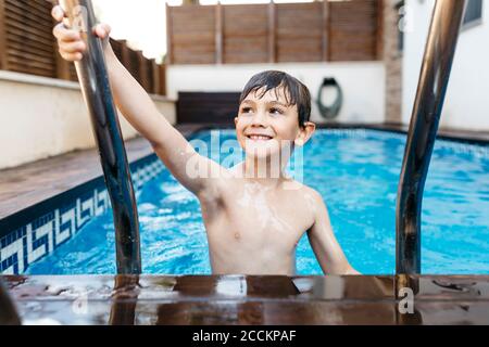 Smiling boy holding ladder in swimming pool