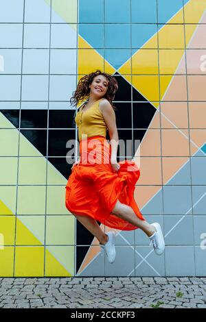 Young woman jumping in front of colorful tiled wall Stock Photo