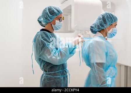 Female doctor tying nurse's protective wear at clinic Stock Photo