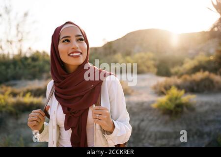 Smiling young tourist woman wearing Hijab in desert landscape looking around Stock Photo