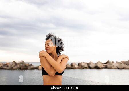 Smiling mid adult woman with eyes closed standing against sea and cloudy sky Stock Photo
