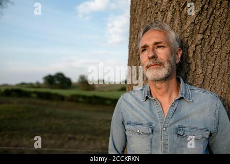 Mature man leaning against a tree trunk in the countryside Stock Photo