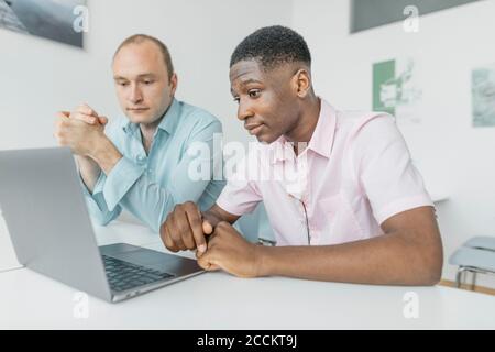Coworkers working on laptop while sitting at workplace Stock Photo