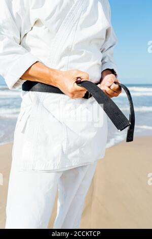 Close-up of mature man tying black belt while standing at beach Stock Photo