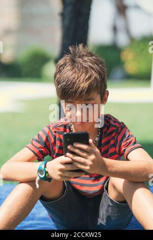 Boy using smart phone while sitting in yard