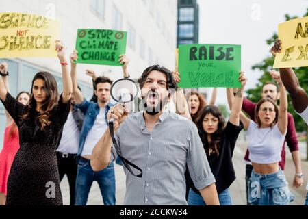Man shouting through megaphone while protesting with people on street Stock Photo