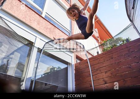 Playful girl jumping on trampoline against house during sunny day