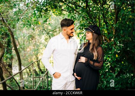 Smiling expectant couple looking at each other while standing in park Stock Photo