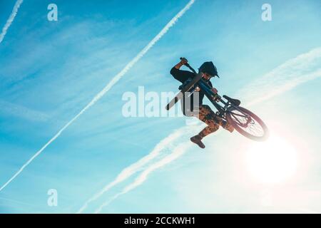 Carefree man jumping while performing stunt with bicycle against blue sky during sunset Stock Photo