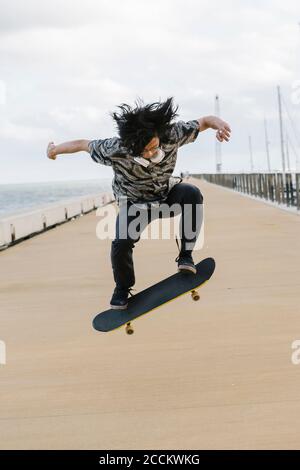 Young man with skateboard performing stunt on promenade against sky Stock Photo