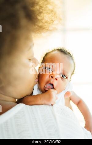 Close-up of mother kissing baby daughter while carrying her at home