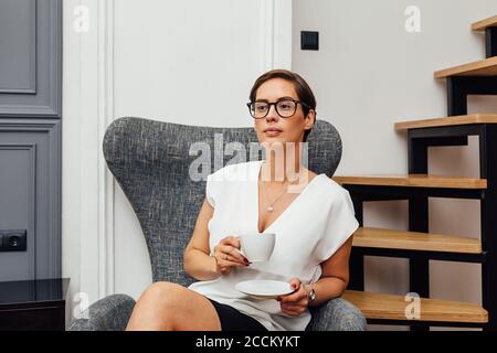 Beautiful mid adult woman drinking coffee in her apartment and looking away Stock Photo