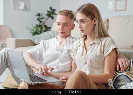 Two young contemporary students sitting on couch in front of laptop display Stock Photo