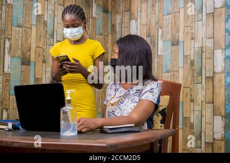Young black female is holding a smartphone while discussing something with her colleague-new normal Stock Photo