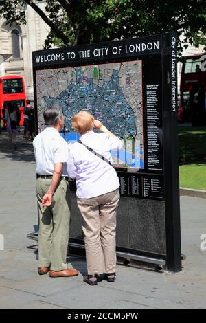 London, UK, July 26, 2014 : Old elderly senior couple reading a tourist welcome information sign map to find a popular travel destination tourist attr Stock Photo