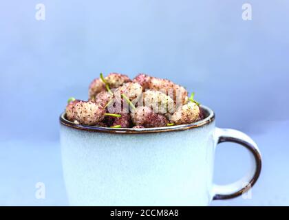 Fresh ripe white mulberry in gray mug on light blue pastel background. Healthy breakfast concept. Summer seasonal fruits. Selective focus Stock Photo