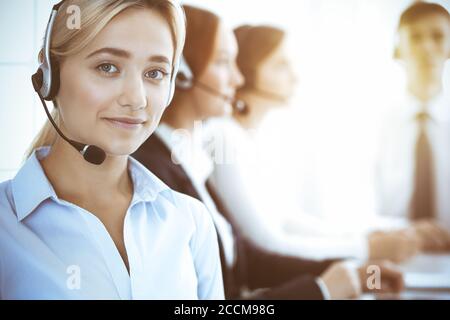 Call center and business people concept. Beautiful business woman with headphones consulting clients. Group of diverse phone operators at work in Stock Photo