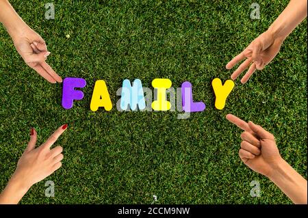 The word 'Family' written with alphabet puzzle letters isolated on grass and hands pointing towards the word representing the family. Stock Photo