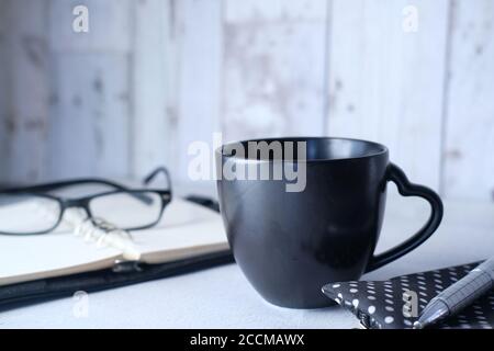 black mug mockup, modern workspace with notepad and eyeglass on table. Stock Photo