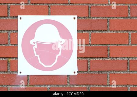 An old, faded hardhat sign on a brick wall. The sign is cracked and faded pink. Stock Photo