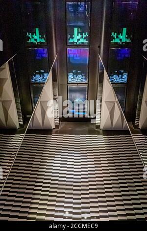 Digital light installations with pixelated green patterns and wave-like blue-light effects decorate a lift lobby at Hotel Blow Up Hall 5050 in Poznań, Poland; the floor is tiled in a black-and-white checkerboard pattern. Stock Photo